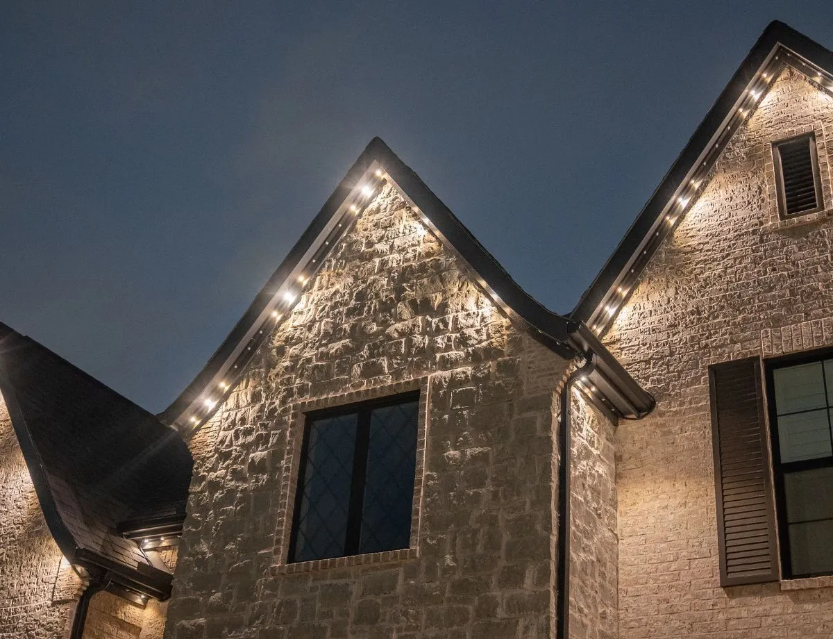 Warm white lights tracing two stone gables at dusk