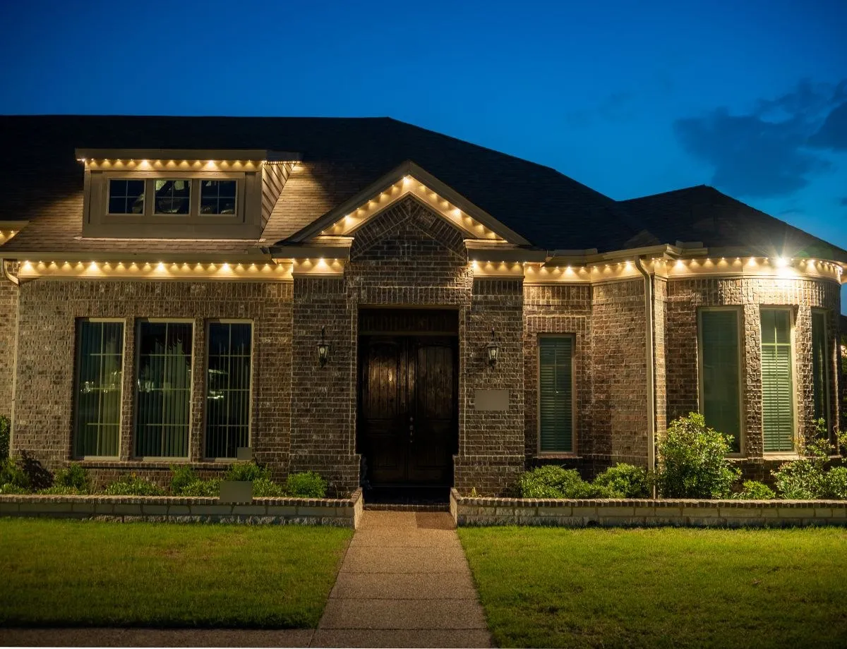 Brick home with warm white lights across the roofline and front entry