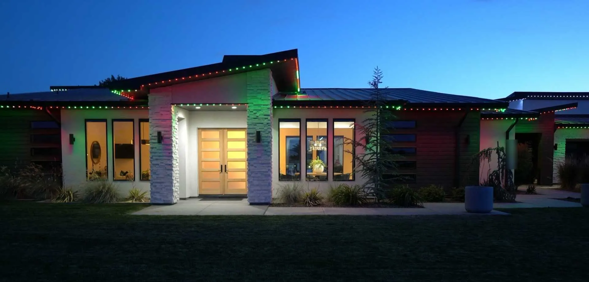 Home with red, green and white Christmas lighting along the roofline at dusk