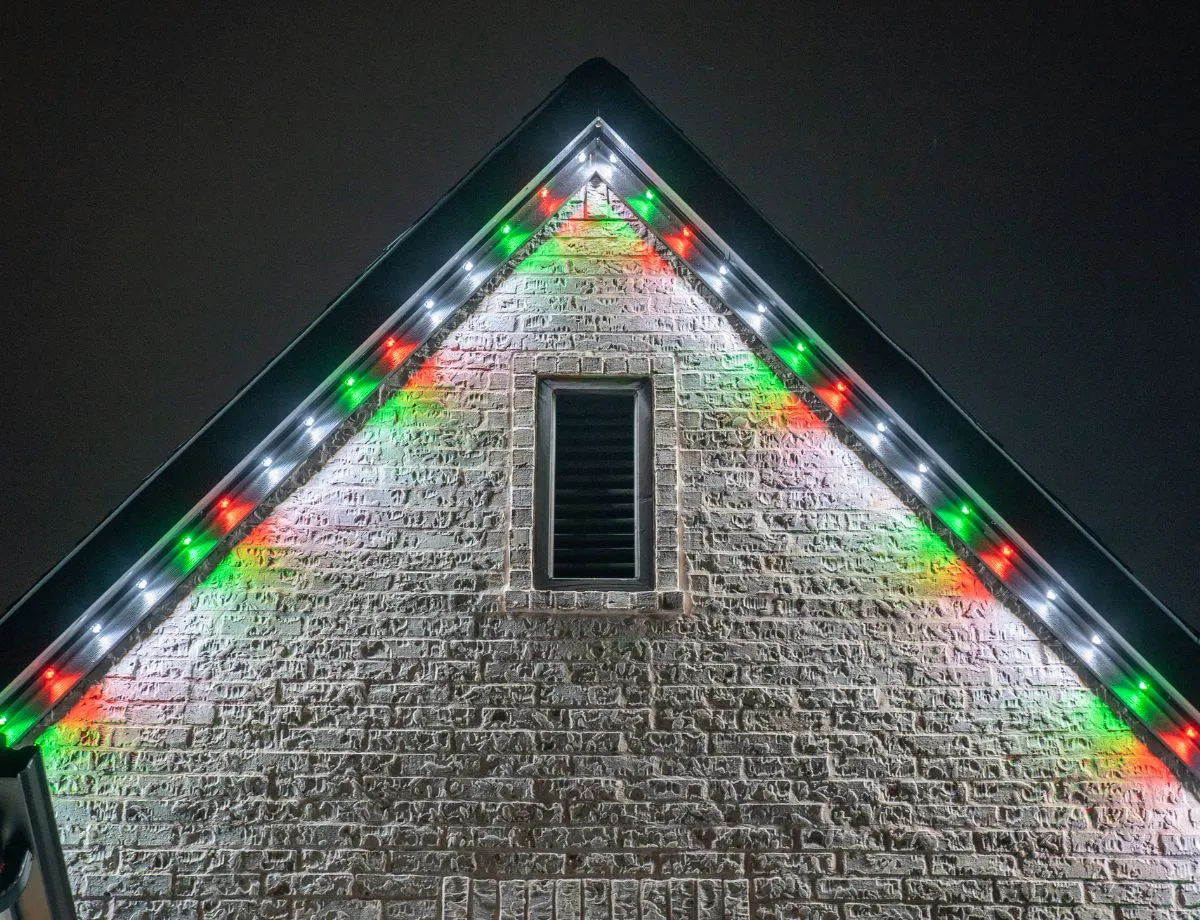 White and green holiday lights tracing a stone gable
