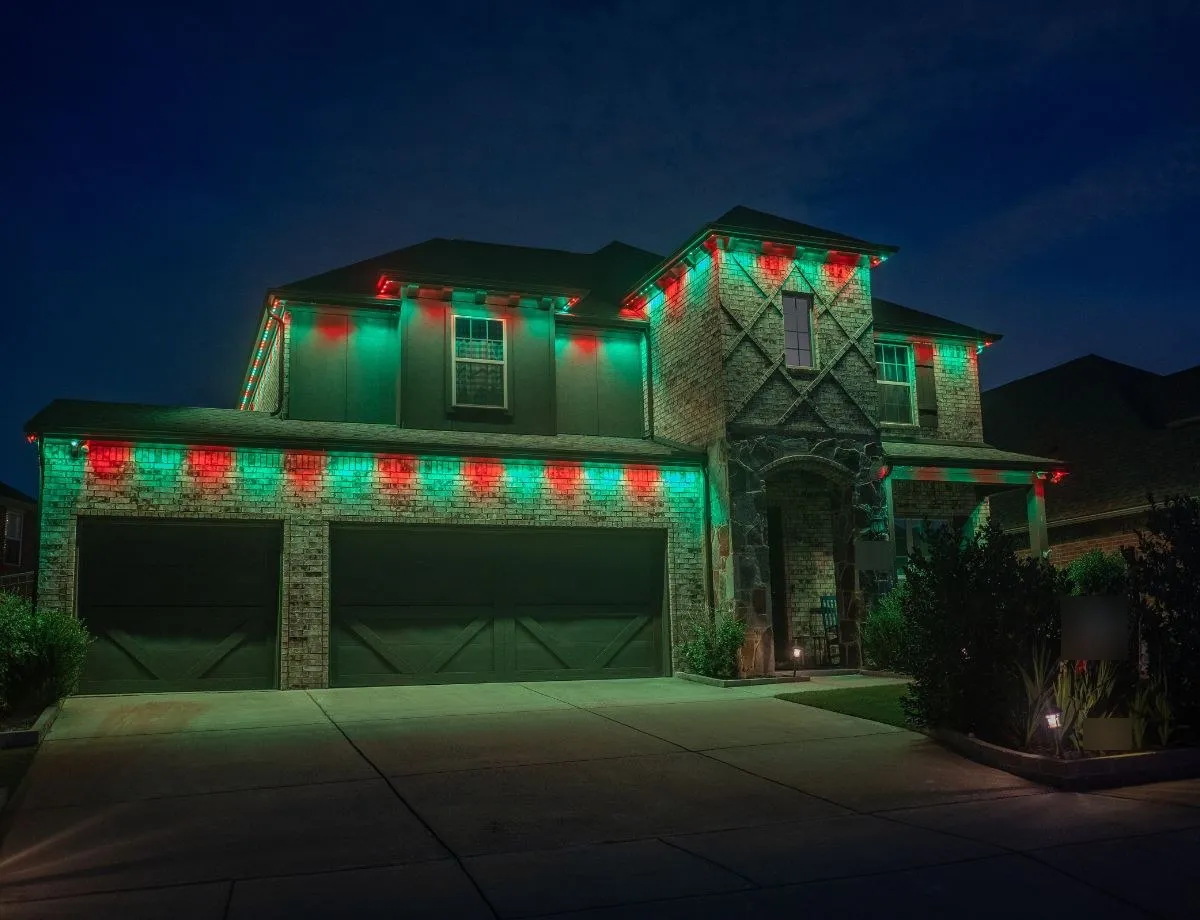 Two-story stone home with red and green holiday lights along the roofline and over the garage