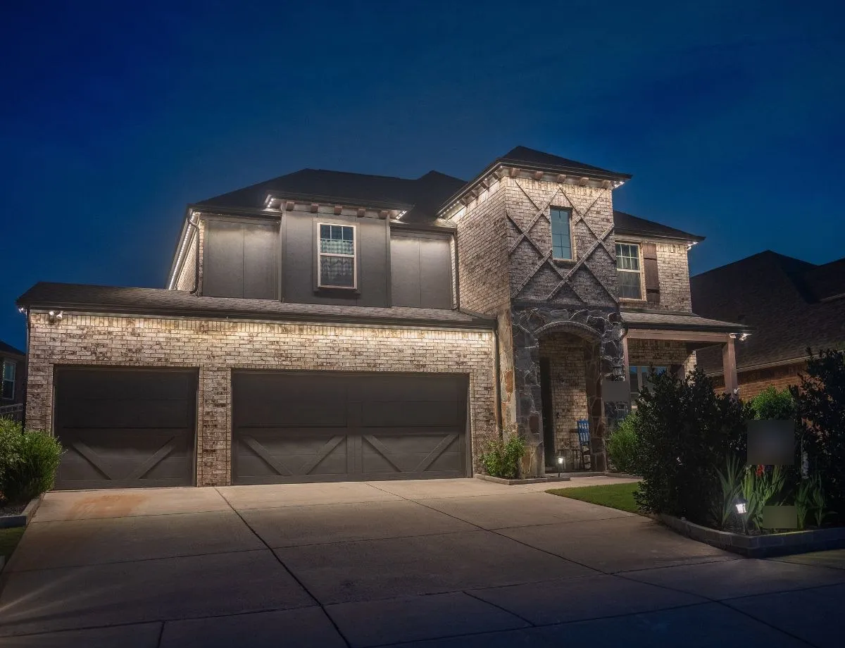Two-car garage and stone entry lit by soft white roofline lights