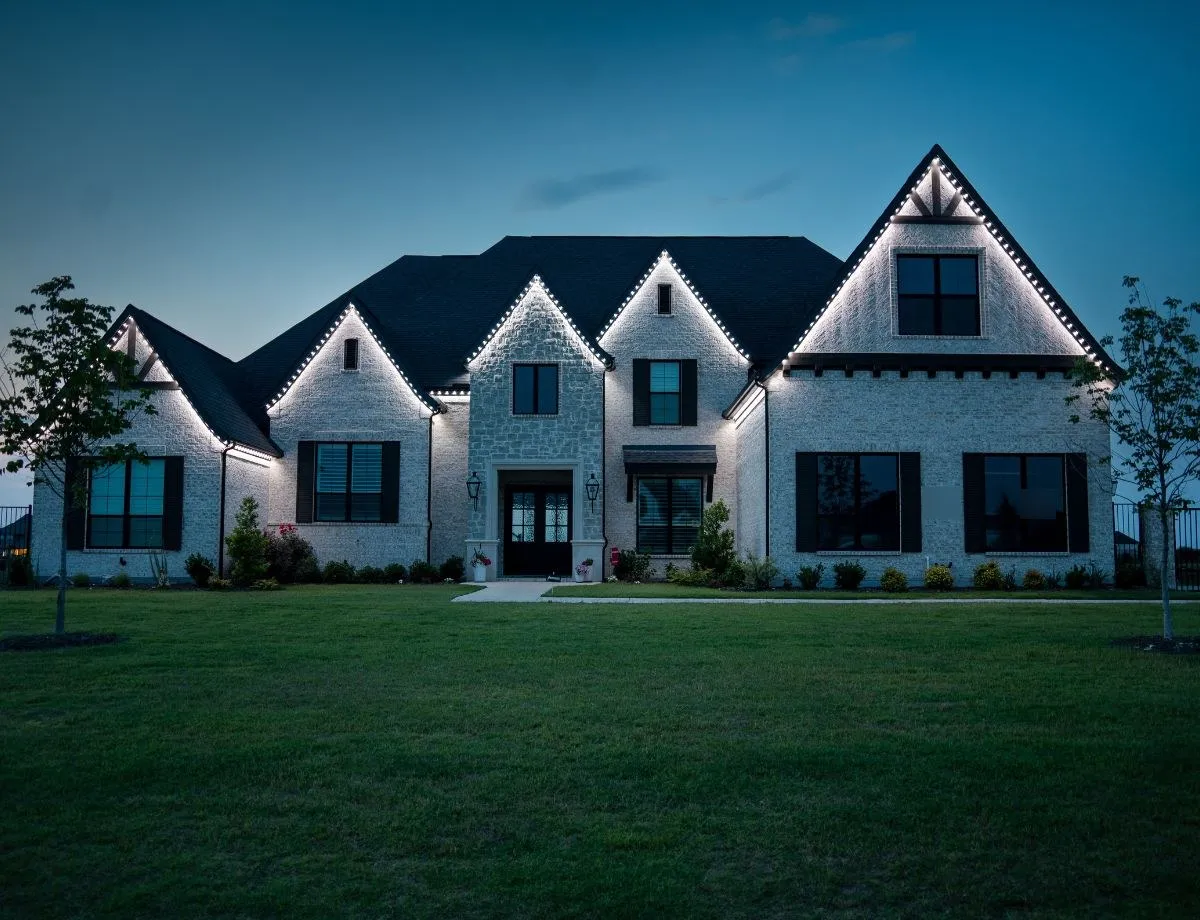 Cool white roofline lights outlining a stone home at night