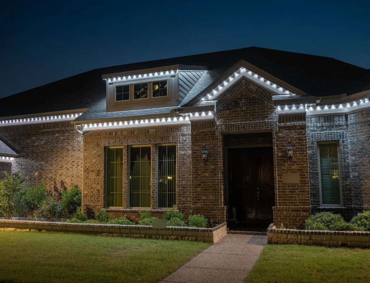 Brick home with bright white lights along the gables and roofline at night