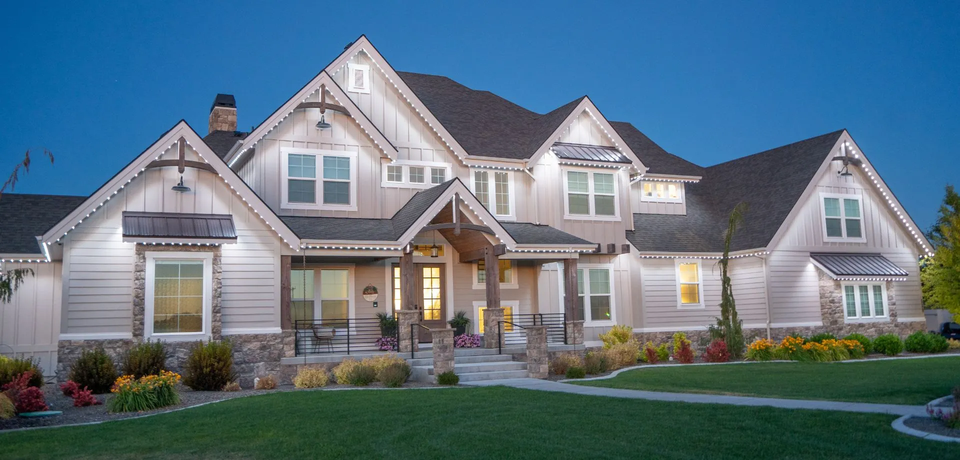 Two-story home with its roofline glowing with permanent lights at dusk